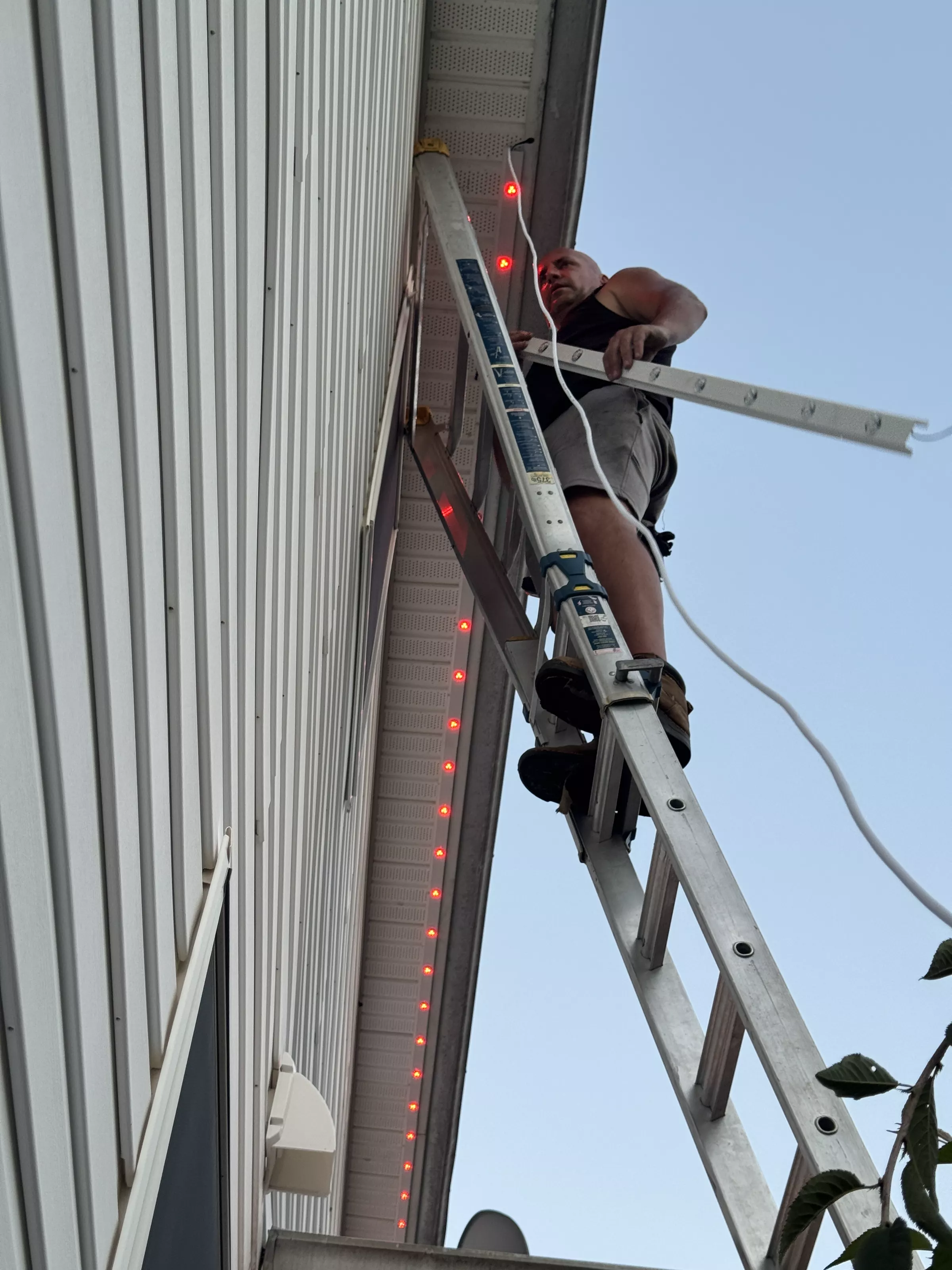 Epic Light installer on a ladder fitting track along a roofline
