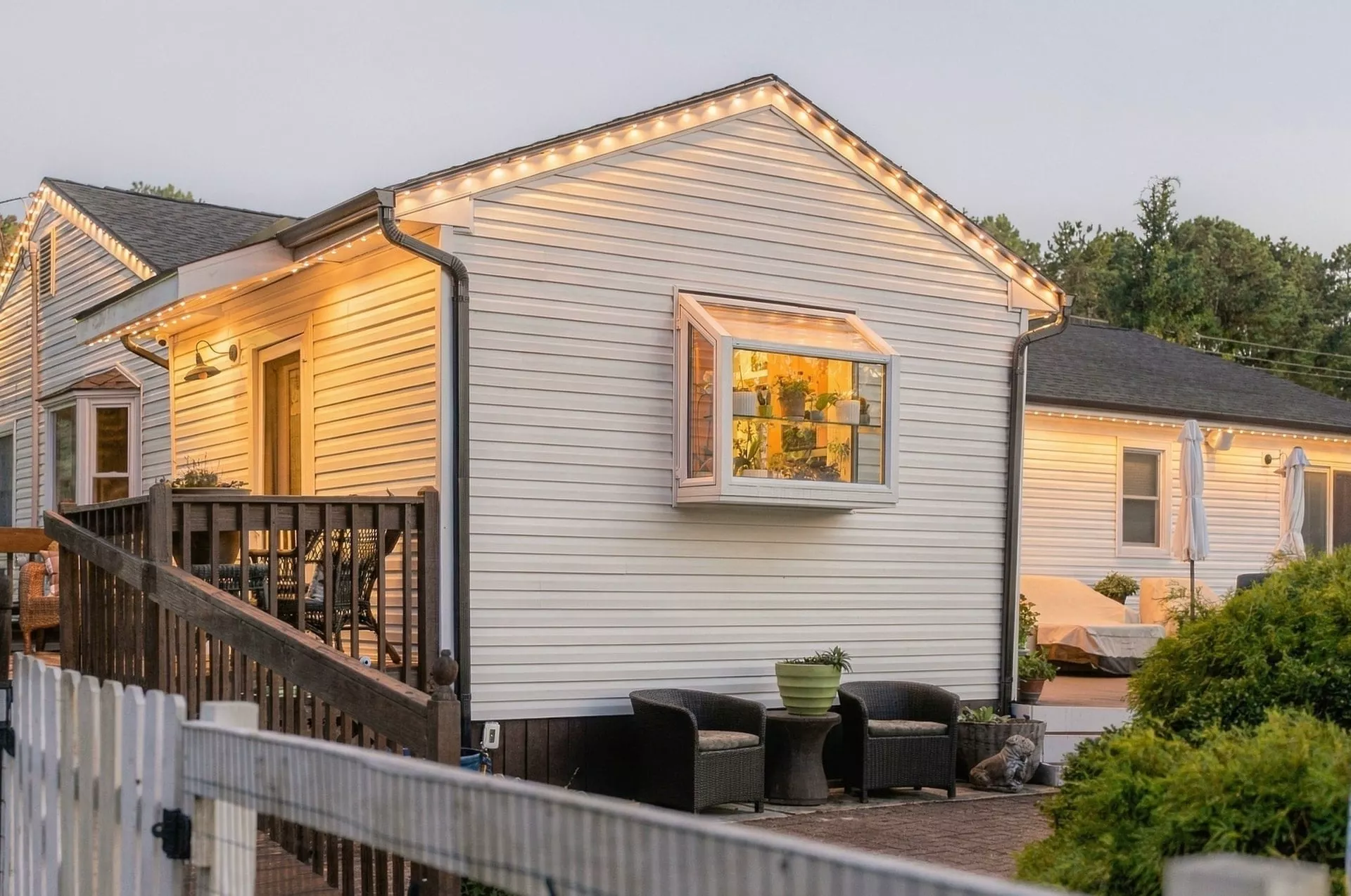 White home with warm roofline lights and a deck at dusk