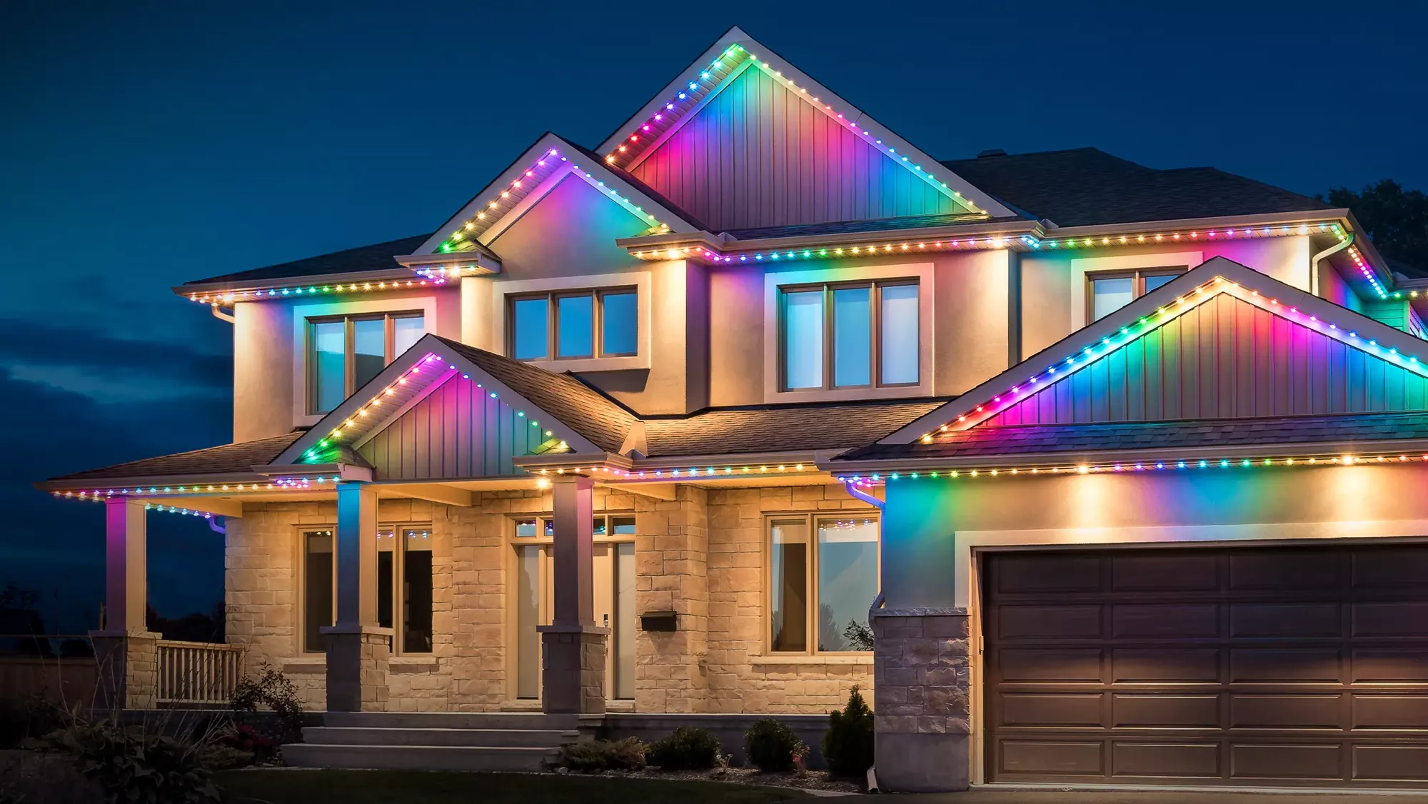 Two-story home with color roofline lights at dusk